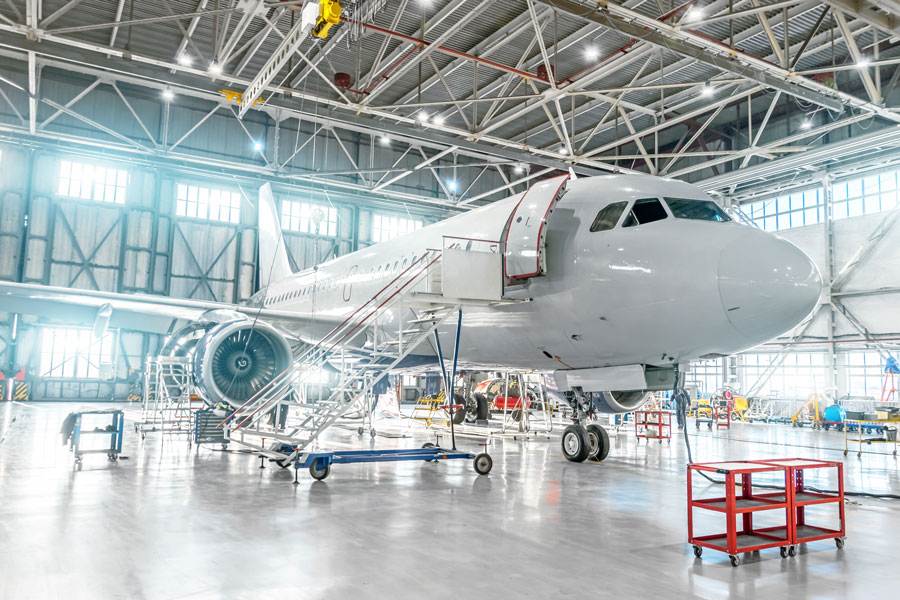 A Commercial Aeroplane In A Bright Hangar, Surrounded By Mechanics, Tools, And Premium Grease Fittings For Global Industries.