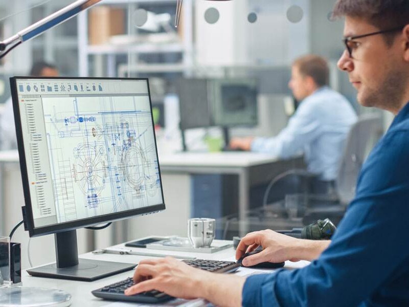 Engineer At A Sleek Office Desk Drafts Grease Nipple Blueprints On Computer, Highlighting Precision Design For Global Industries.