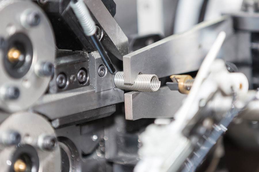 Maquinaria industrial dobla con precisión un resorte de metal, resaltando componentes robustos: fabricación de calidad para clientes globales de engrasadores.