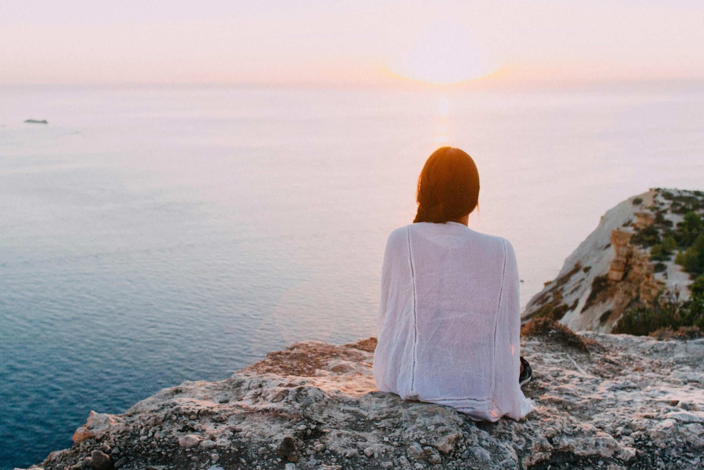 Una mujer sentada en una roca mirando la puesta de sol