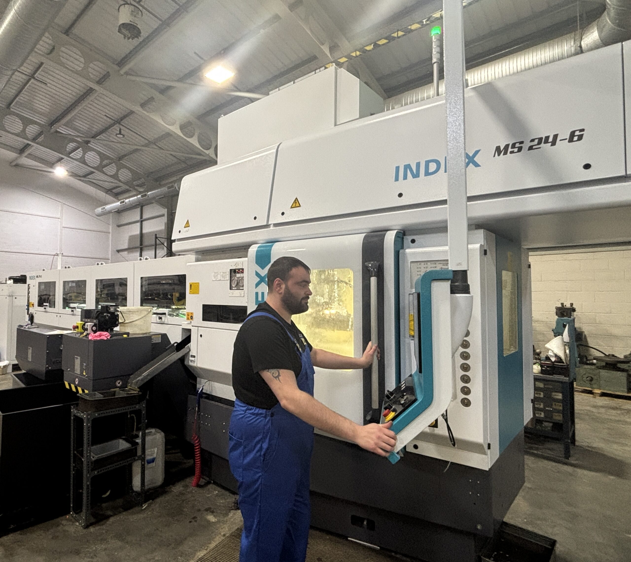 Skilled Technician In Blue Overalls Uses Advanced Cnc Machine In Bright Factory, Highlighting Precision Grease Nipple Manufacturing.